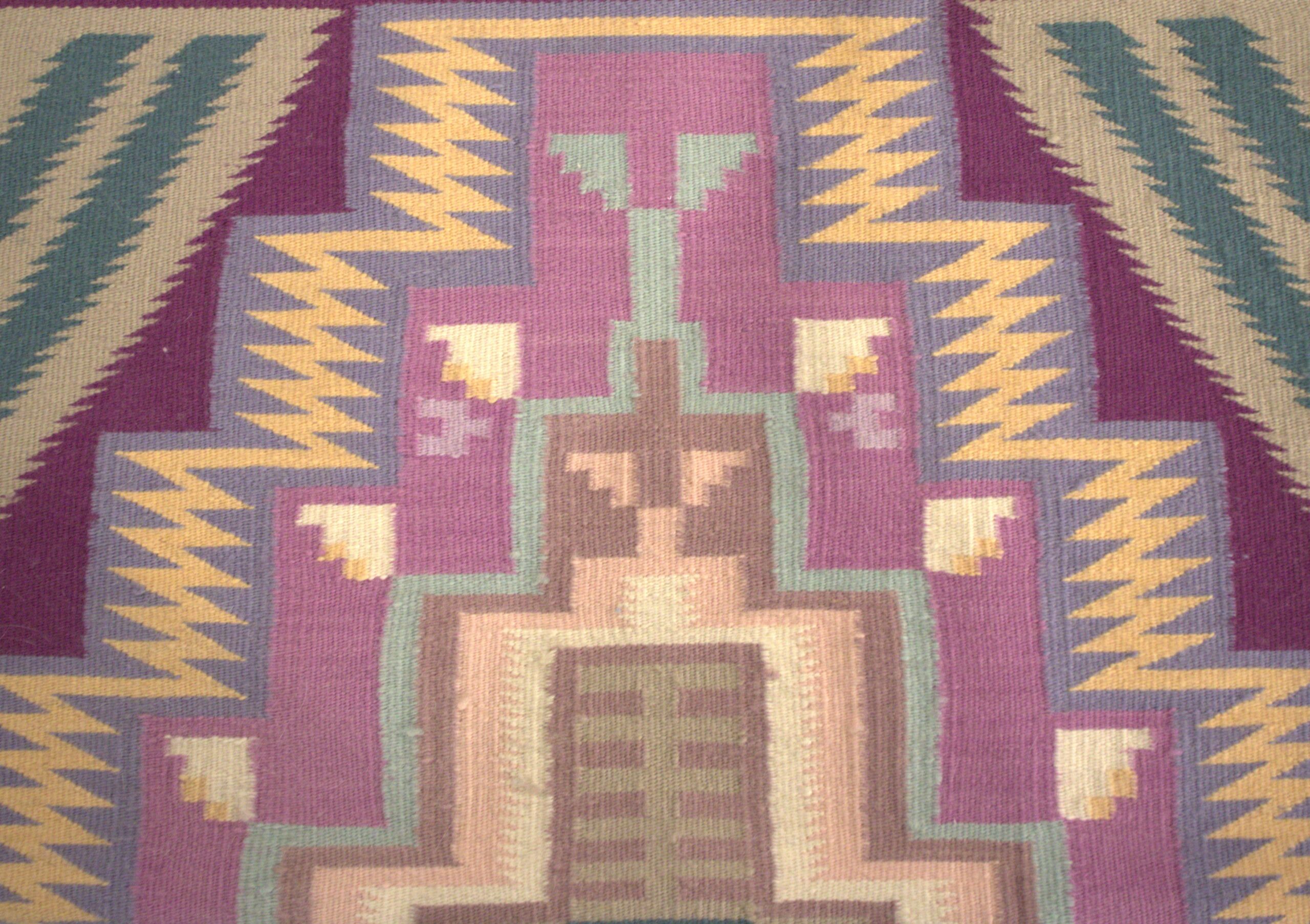 Colorful woven rug with geometric tribal patterns in purple, teal, yellow, and beige edge detailing.