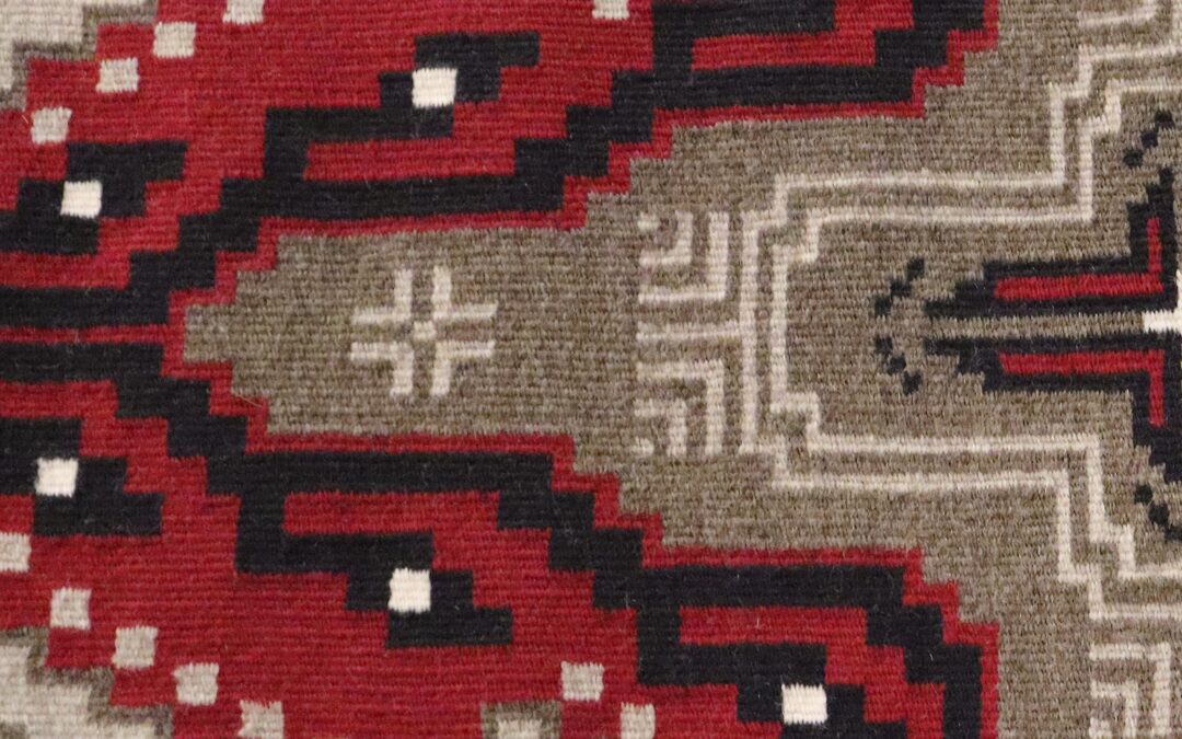 Close-up of a geometric patterned rug with red, black, beige, and white shapes.