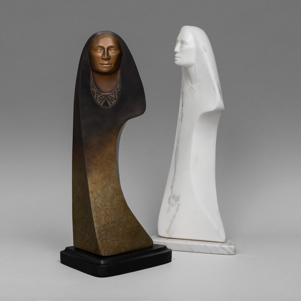 Two abstract sculpture busts: a dark brown figure with a carved necklace beside a white marble figure, both on stands against a gray backdrop.